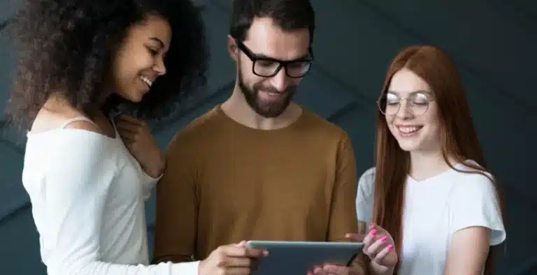 Três pessoas olhando um tablet e sorrindo