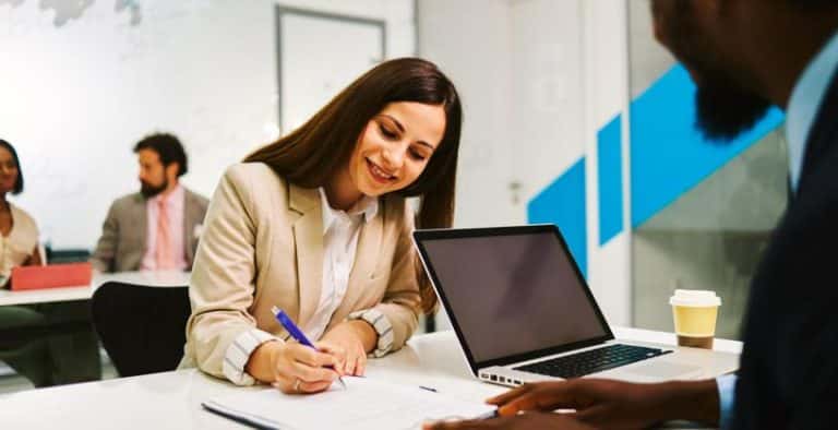 Mulher sentada em uma mesa, assinando um contrato intermitente.